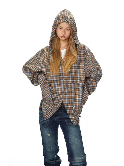 A young woman with long blonde hair wearing a plaid hooded jacket and blue jeans stands with her hands on her hips, looking directly at the camera.