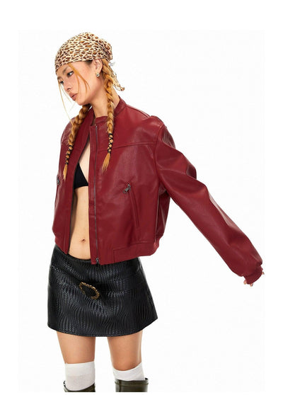 A woman wearing a red leather jacket, a black skirt, and a leopard print headband stands with her arm outstretched.