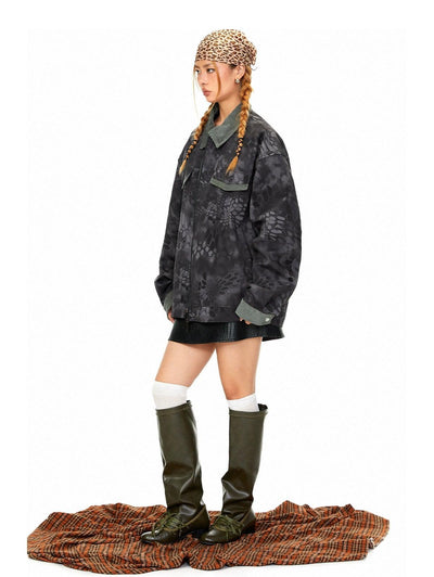 A person wearing a black jacket with a camouflage pattern, a leopard print hat, a black skirt, and olive green boots stands on a plaid blanket.