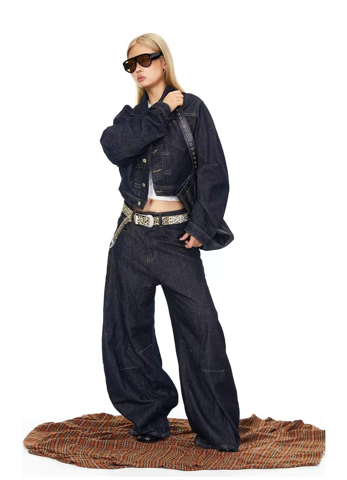 A woman wearing a denim jacket, sunglasses, and wide-leg jeans stands on a striped blanket.