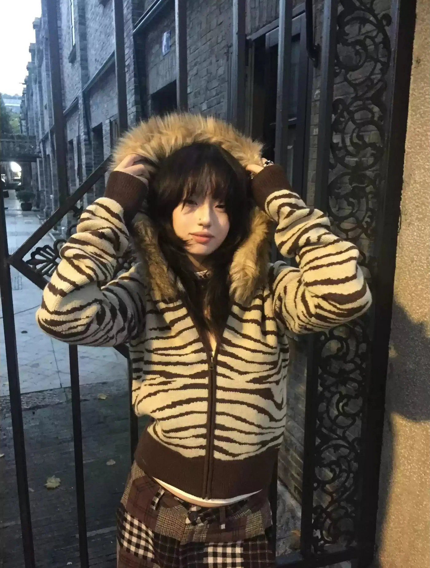 a woman standing in front of a gate wearing a zebra print jacket