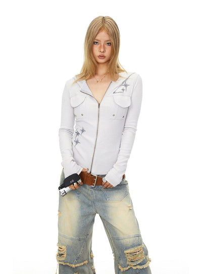 A young woman with long blonde hair is standing against a white background, wearing a white long-sleeved shirt with a zipper and a brown belt. She is also wearing distressed jeans.