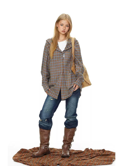A young woman with long blonde hair stands confidently, wearing a plaid shirt, jeans, and brown boots, with a beige bag slung over her shoulder.